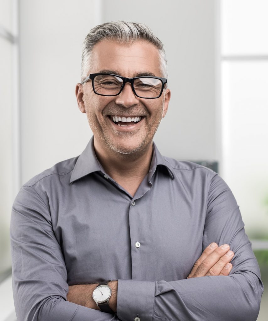 a smiling man with glasses and a gray shirt.
